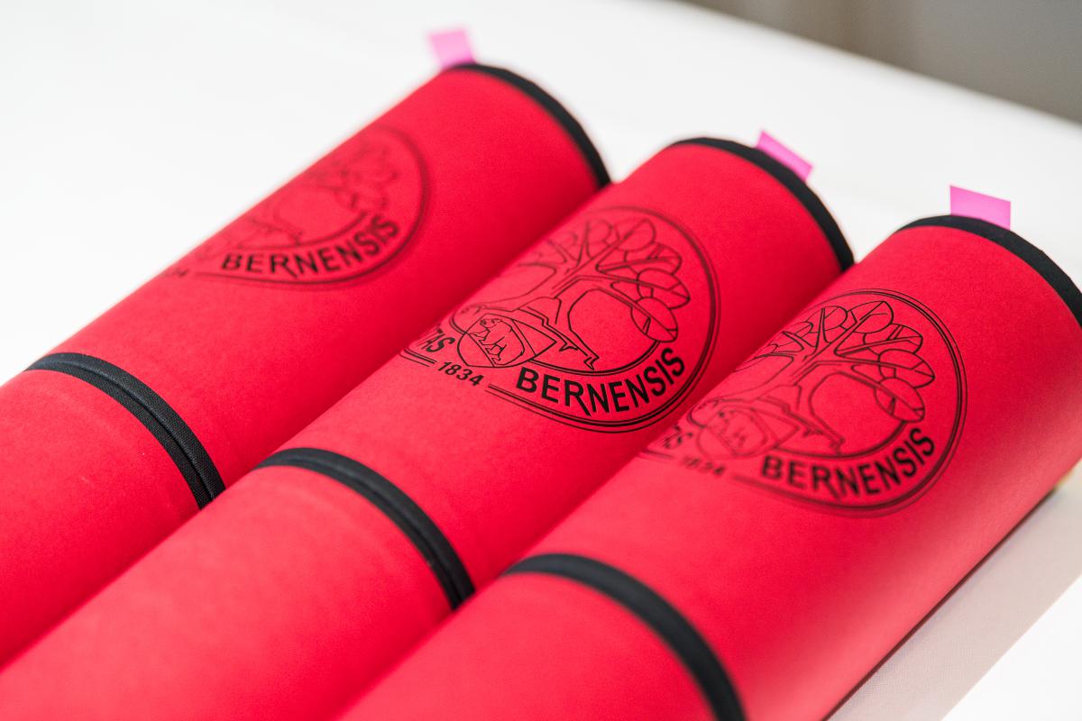 Dies academicus 2023 – drei rote Diplomrollen mit pink farbigen Post-it markiert.  © Universität Bern
